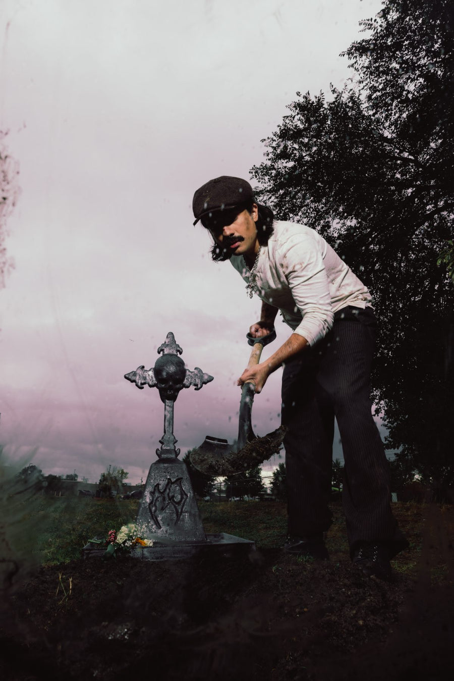 Digging a grave beside a skull cross headstone in the rain